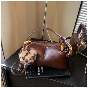 Detail of dark brown cylindrical crossbody bag with leopard heart charm on a book