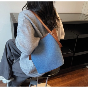Detail of denim and leather bucket bag worn on shoulder by model in a minimalist room