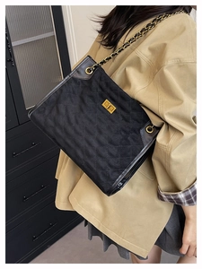 Détail d'un sac cabas en daim noir matelassé avec bandoulière chaîne dorée et fermoir