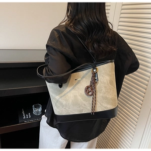 Detail of taupe suede tote bag with black leather trim and decorative knotted charm