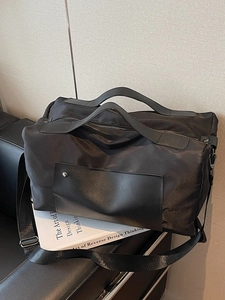 Large black nylon travel bag with handles and wide shoulder strap on a sleek sofa