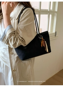 Detail of black suede tote bag featuring a retro wooden bead tassel and slim shoulder strap