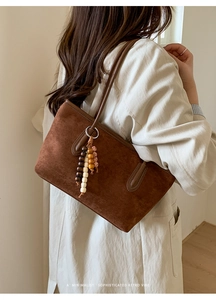 Detail of dark brown suede tote bag with wooden bead charm in a minimalist setting