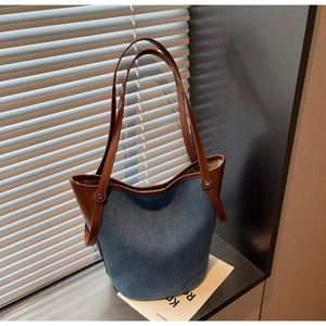 Detail of denim bucket bag with brown leather trim and silver metal rivets on side