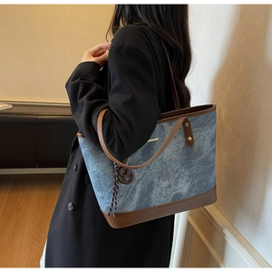 Detail of blue denim tote bag with brown leather handles and gold logo bar on the side