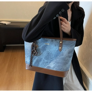 Detail of denim tote bag with brown leather trim and heart charm held by a model