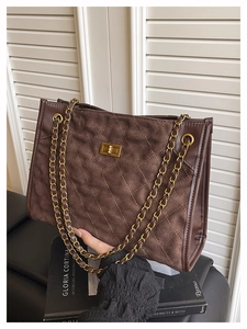 Détail d'un sac cabas en daim matelassé marron avec fermoir doré et bandoulière chaîne