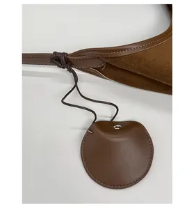 Close-up of brown matte leather shoulder bag showing stitching and round pendant detail