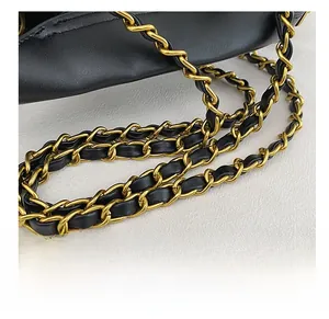 Close-up of elegant gold metal chain woven with black leather strap on a bucket bag
