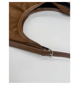 Detail of adjustable shoulder strap buckle on a brown suede bucket bag