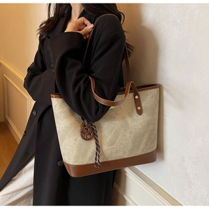 Detail view of large tote bag with contrast brown straps and decorative round charm