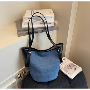 Detailed close-up of blue denim bucket tote bag with black leather straps and metal rivets