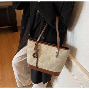 Detail of grey fabric and brown leather tote bag with stylish charm on model