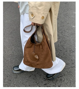 Detail of a large brown suede hobo bag with side circular leather pendant and tie strap