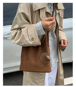 Brown matte suede bucket bag with round pendant shown on shoulder in outdoor street setting