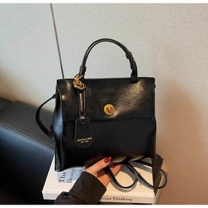 Detail of a vintage black leather handbag with a gold twist lock and a round brand tag