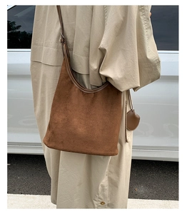 Close-up of brown suede hobo shoulder bag with leather trim and round charm detail