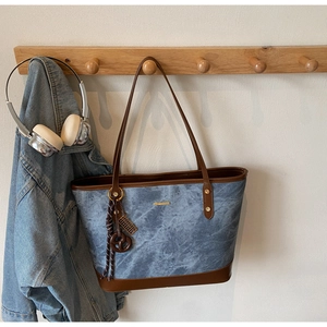 Detail of denim texture tote bag with brown leather trim and metal bar on wooden hook