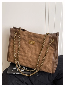 Détail du sac cabas en daim marron avec bandoulière chaîne dorée et fermoir pivotant