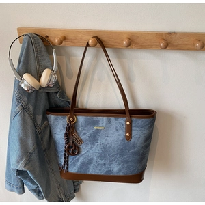 Detail of a denim tote bag with brown leather trim hanging on a wooden hanger with jacket