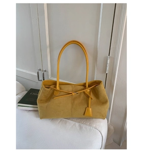 Dettaglio di una borsa tote gialla in pelle opaca su un divano bianco in casa