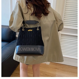 Detail of black quilted suede bucket bag with gold lock and branded leather base