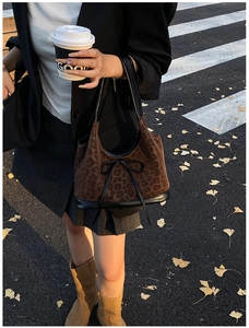 Detail view of leopard print bucket bag with black glossy trim and bow on urban street