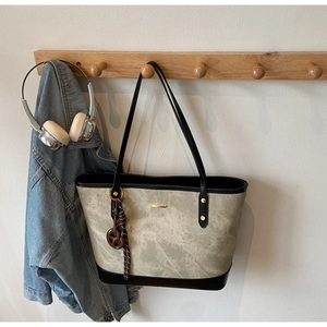 Detail of marble texture tote bag with black leather straps and pretzel charm on a wooden hook
