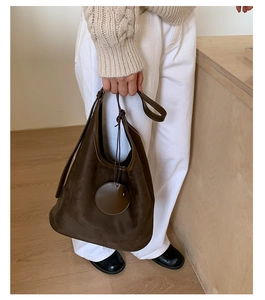 Detail of dark brown suede bucket bag featuring a minimalist strap and round charm