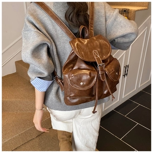 Detail view of a vintage brown leather backpack with buckle pockets and white stitching