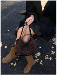 Brown leopard print tote bag featuring black leather trim and bow detail on a park bench