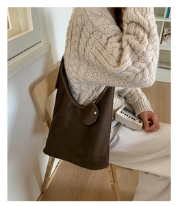 Detail of dark brown suede tote bag with decorative leather charm in an autumn setting