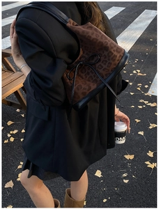 Outdoor view of a leopard print hobo bag with black leather trim and bow detail