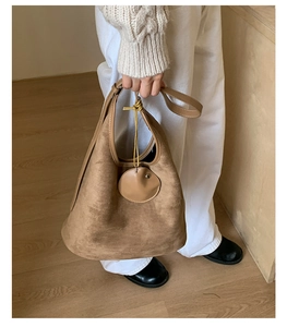Brown suede shoulder bag with smooth leather trim details shown in a minimalist setting