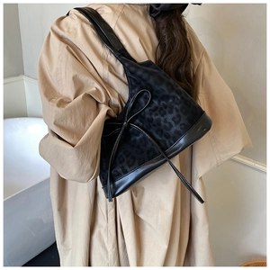 Detailed side view of leopard print bucket bag with leather bow on model in beige dress