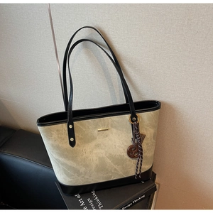 Detail of stone textured tote bag featuring black leather trim and decorative bag charm