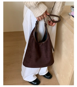 Detail of a large dark brown suede tote bag with leather straps on a warm neutral background