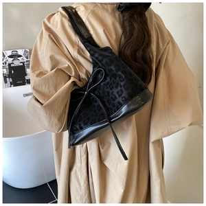 Detailed view of leopard print bucket bag with black leather trim and bow detail on model