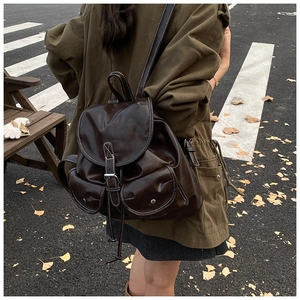 Detail of dark brown leather backpack with contrast stitching and metal snap pockets
