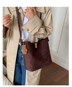 Detail of dark brown suede bucket bag featuring a gold twist lock and plush bear charm