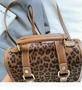 Close-up of leopard print handbag showing brown leather handles and gold metal buckles
