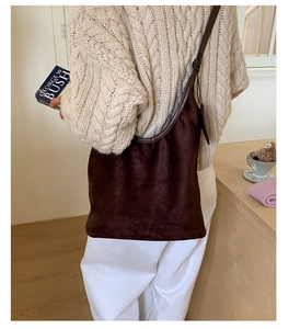 Brown faux suede hobo bag shown on shoulder in a warm lifestyle interior setting