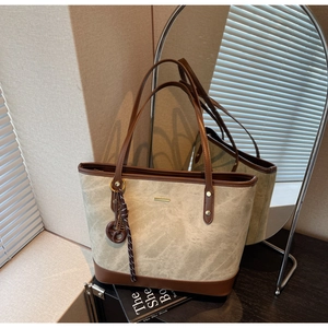 Detail of vintage tote bag featuring brown leather trim and metal pendant decoration