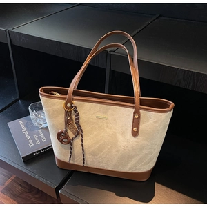 Detail of minimalist tote bag with smooth brown leather trim and pretzel charm accessory