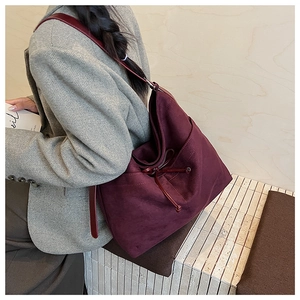 Detail view of large burgundy suede tote bag with decorative drawstrings on model