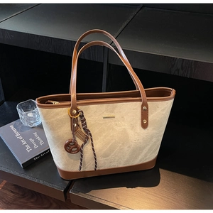 Detail of canvas tote bag with brown leather trim and creative biscuit pendant decoration
