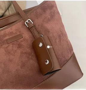Detail of suede tote bag showing leather stitching, silver buckles and hanging accessory
