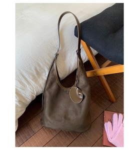 Detailed close-up of brown suede hobo bag featuring a round decorative tag and slim strap