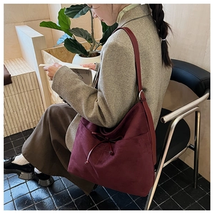 Detail of burgundy suede tote bag with drawstring, shown in a casual lifestyle setting
