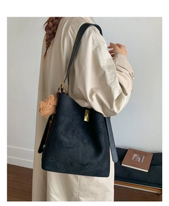 Detail of black suede bucket bag with gold square buckle and brown plush bear charm